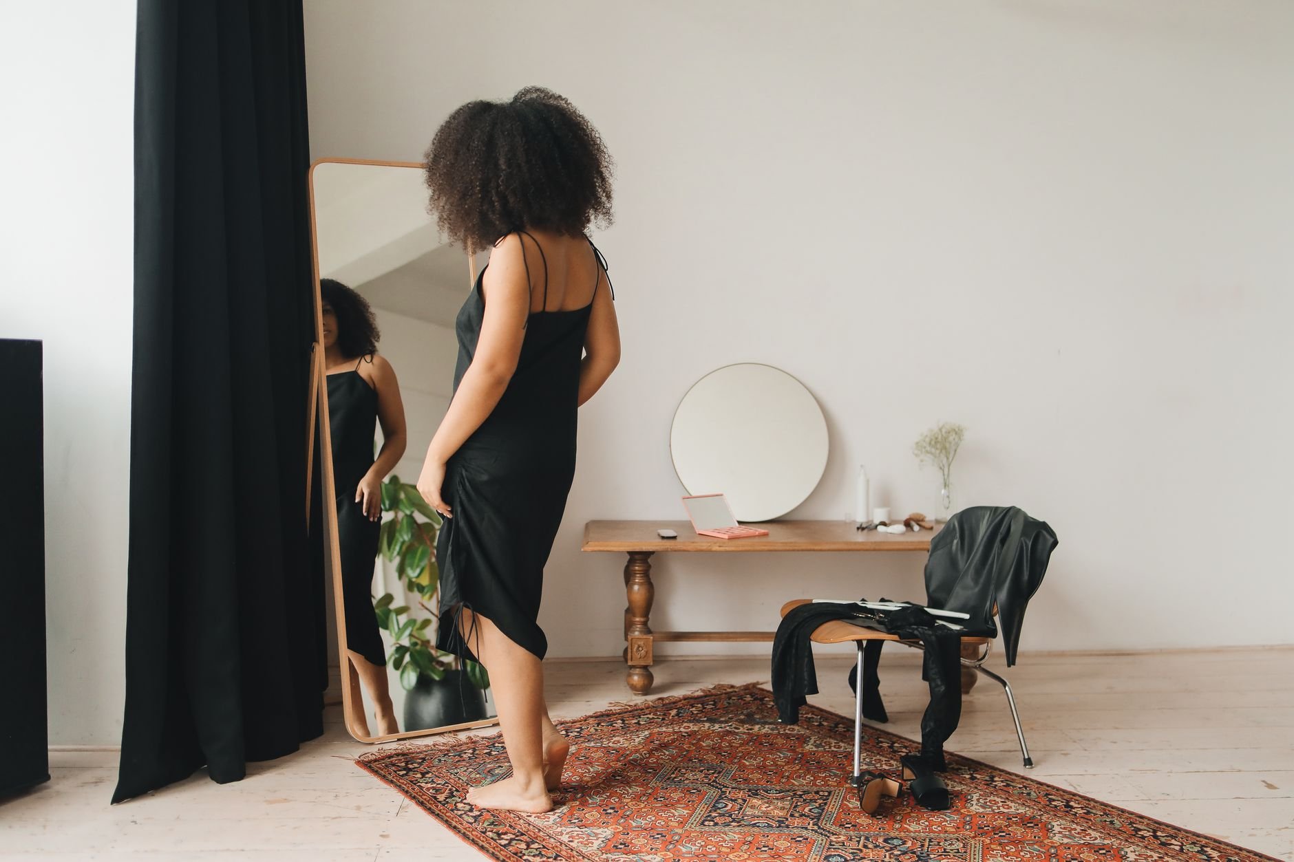 Woman in elegant black dress getting ready in front of mirror — personal styling moment
